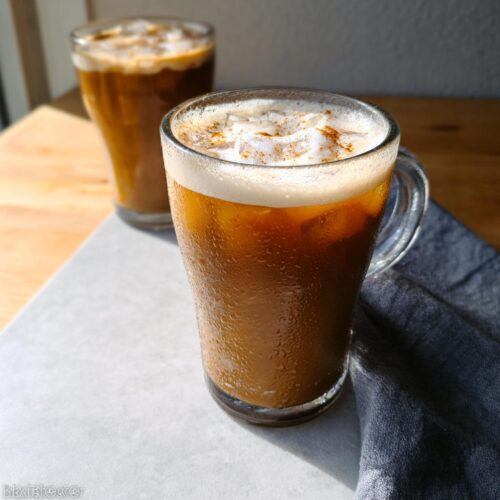 Close-up of a frosty glass containing a Vegan Iced Chai Tea Latte topped with foam and cinnamon.