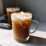 Close-up of a frosty glass mug filled with Vegan Iced Chai Tea Latte, ice, and creamy foam topping.
