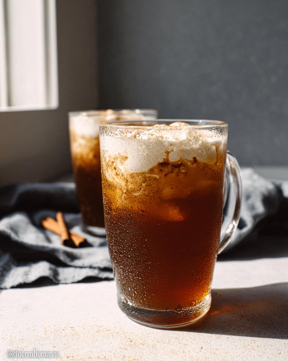 Close-up of a frosty glass mug filled with Vegan Iced Chai Tea Latte, topped with creamy foam and cinnamon.