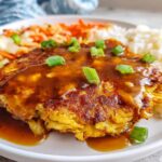 Close-up of a golden-brown Vegetable Egg Foo Young patty covered in savory brown sauce and green onions.