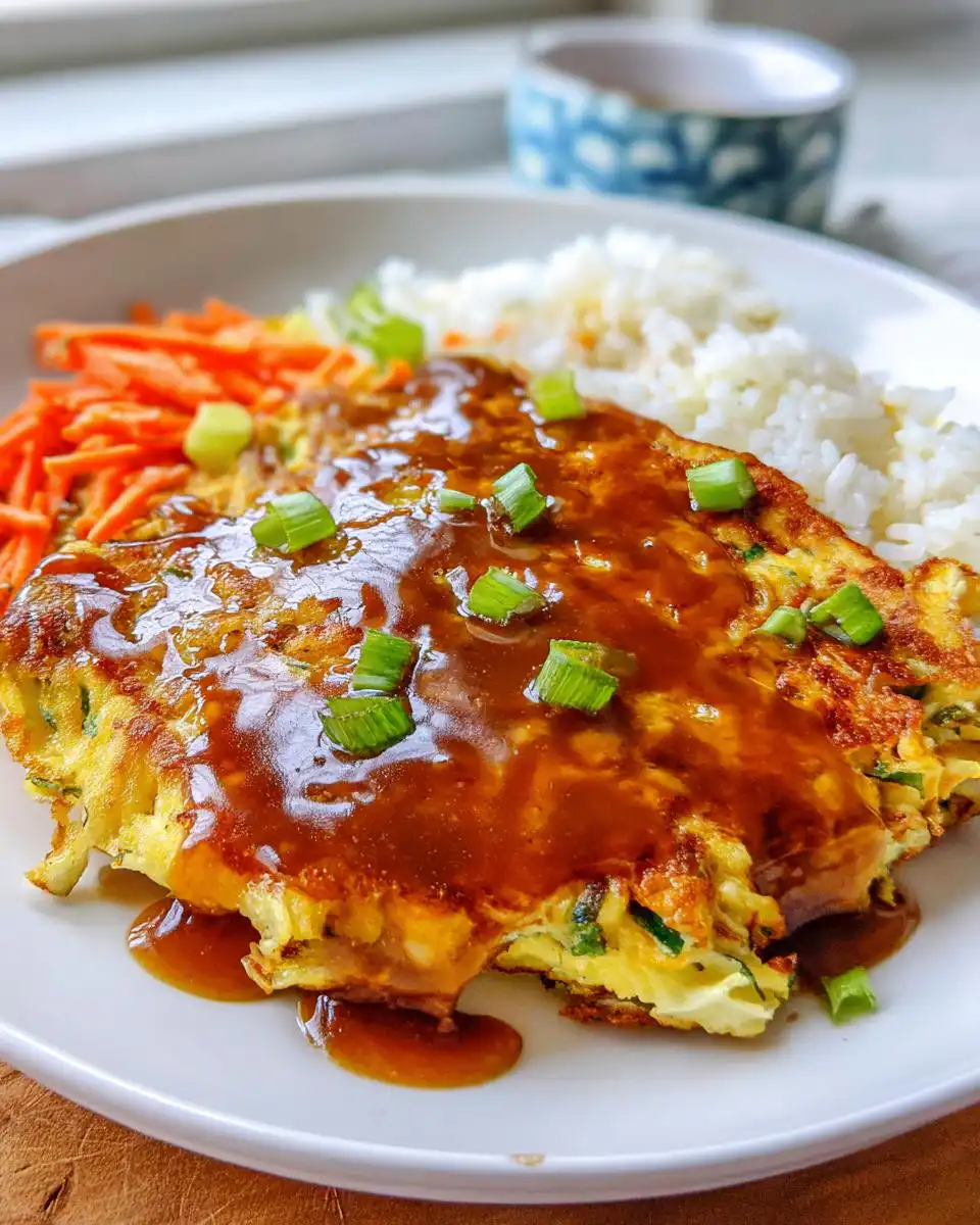 A plate featuring Vegetable Egg Foo Young smothered in brown gravy, served with white rice and shredded carrots.