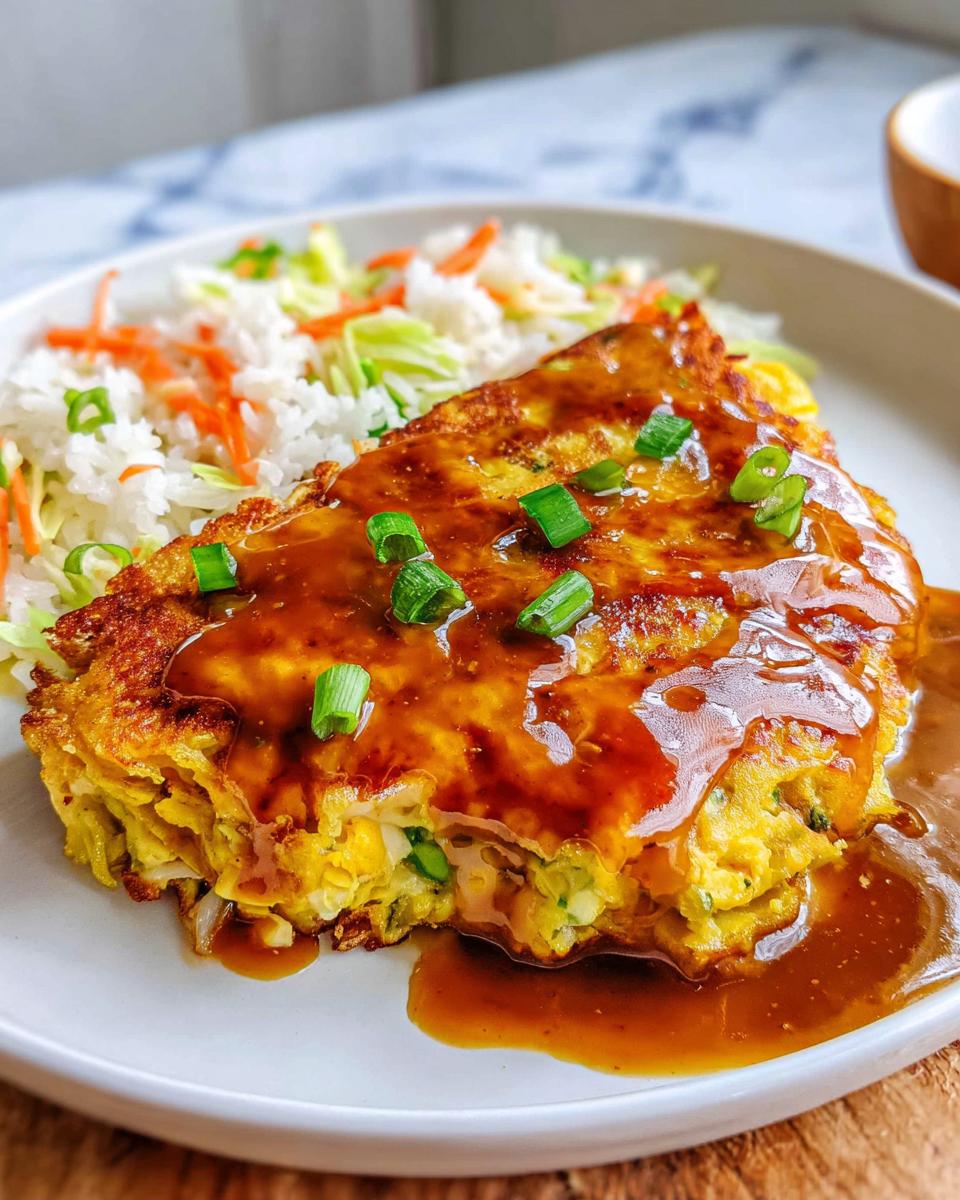 A serving of Vegetable Egg Foo Young, smothered in brown gravy and topped with green onions, served alongside rice.