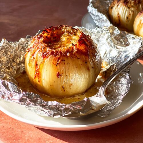 A close-up of a perfectly cooked Viral Foil-Wrapped Onion Boil sitting in its juices on a plate with a spoon.