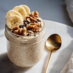A jar of Blended Banana Bread Overnight Oats topped with sliced bananas, walnuts, and chocolate chips.