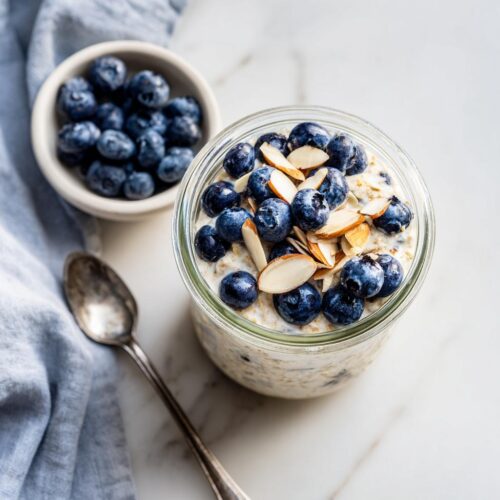 Overhead view of Blueberry Almond Overnight Oats topped with fresh blueberries and sliced almonds in a glass jar.