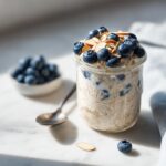 A jar filled with Blueberry Almond Overnight Oats, topped with fresh blueberries and sliced almonds.