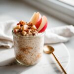 A jar filled with Brown Sugar Apple Overnight Oats, topped with diced apples, nuts, and cinnamon.