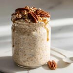 A glass jar filled with creamy Brown Sugar Pecan Overnight Oats, topped with whole pecans and drizzled with syrup.