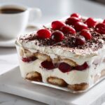 Layers of Cherry Coconut Cream Tiramisu without mascarpone, topped with fresh cherries and chocolate shavings.