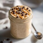 A jar filled with creamy Cookie Dough Blended Overnight Oats, topped with peanut butter drizzle and chocolate chips.