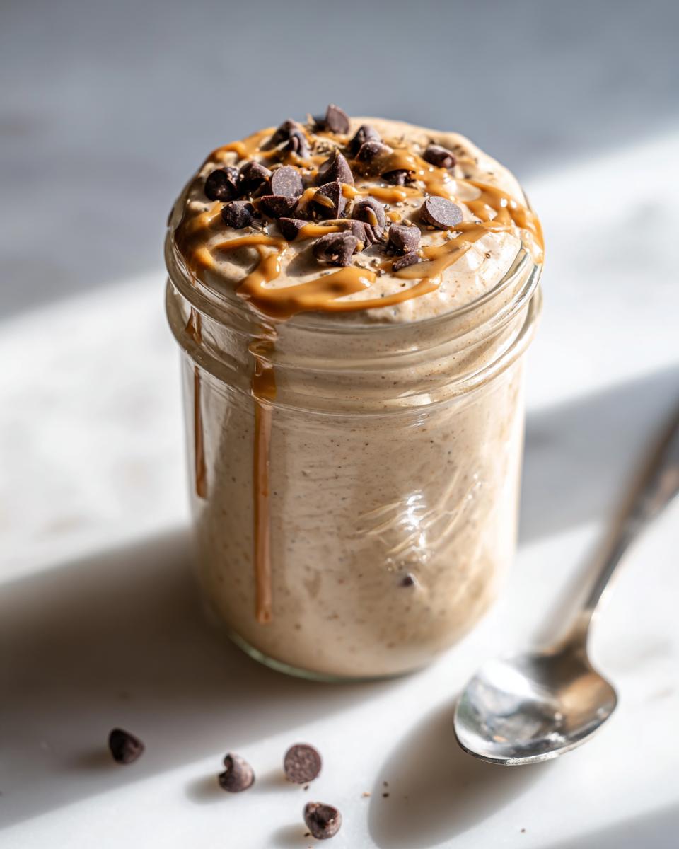Close-up of Cookie Dough Blended Overnight Oats topped with chocolate chips and caramel drizzle in a jar.