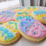 Several oval-shaped Easter Sugar Cookies with Pastel Icing featuring yellow, pink, and lavender frosting designs.