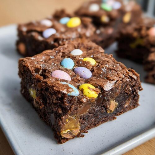 A close-up of a fudgy Cadbury Egg Brownies square topped with colorful mini eggs and sparkling sugar.