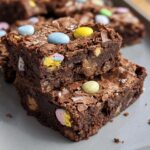 Two fudgy Cadbury Egg Brownies stacked on a grey plate, topped with colorful mini chocolate eggs.