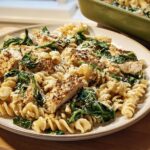 A plate of Healthy Garlic Parmesan Chicken Pasta with Spinach, featuring rotini pasta, sliced chicken breast, and wilted spinach.