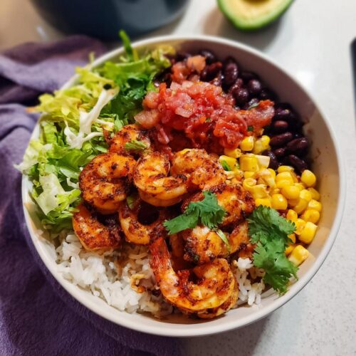Close-up of a High Protein Shrimp Taco Bowl featuring seasoned shrimp, rice, black beans, corn, salsa, and lettuce.