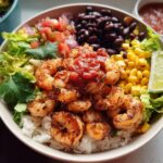 Close-up of a vibrant High Protein Shrimp Taco Bowl featuring seasoned shrimp over rice, black beans, corn, salsa, and lettuce.