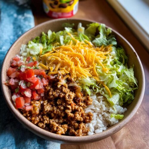 A close-up of a High Protein Turkey Taco Bowl featuring seasoned ground turkey, white rice, shredded lettuce, cheese, and pico de gallo.