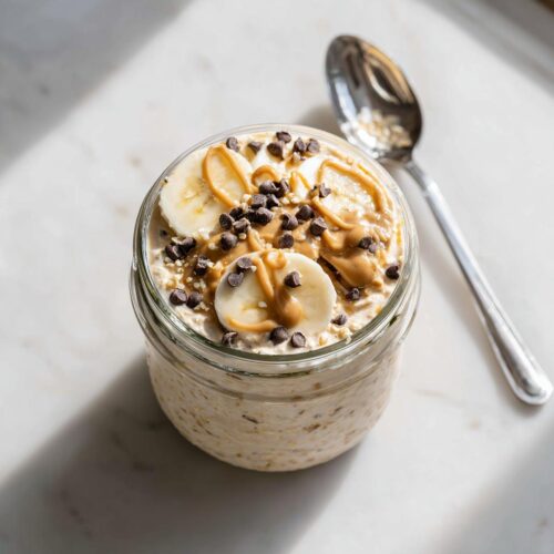 Overhead view of Peanut Butter Banana Cinnamon Overnight Oats topped with banana slices, peanut butter drizzle, and mini chocolate chips.