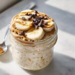 Close-up of Peanut Butter Banana Cinnamon Overnight Oats topped with banana slices, peanut butter drizzle, and chocolate chips.