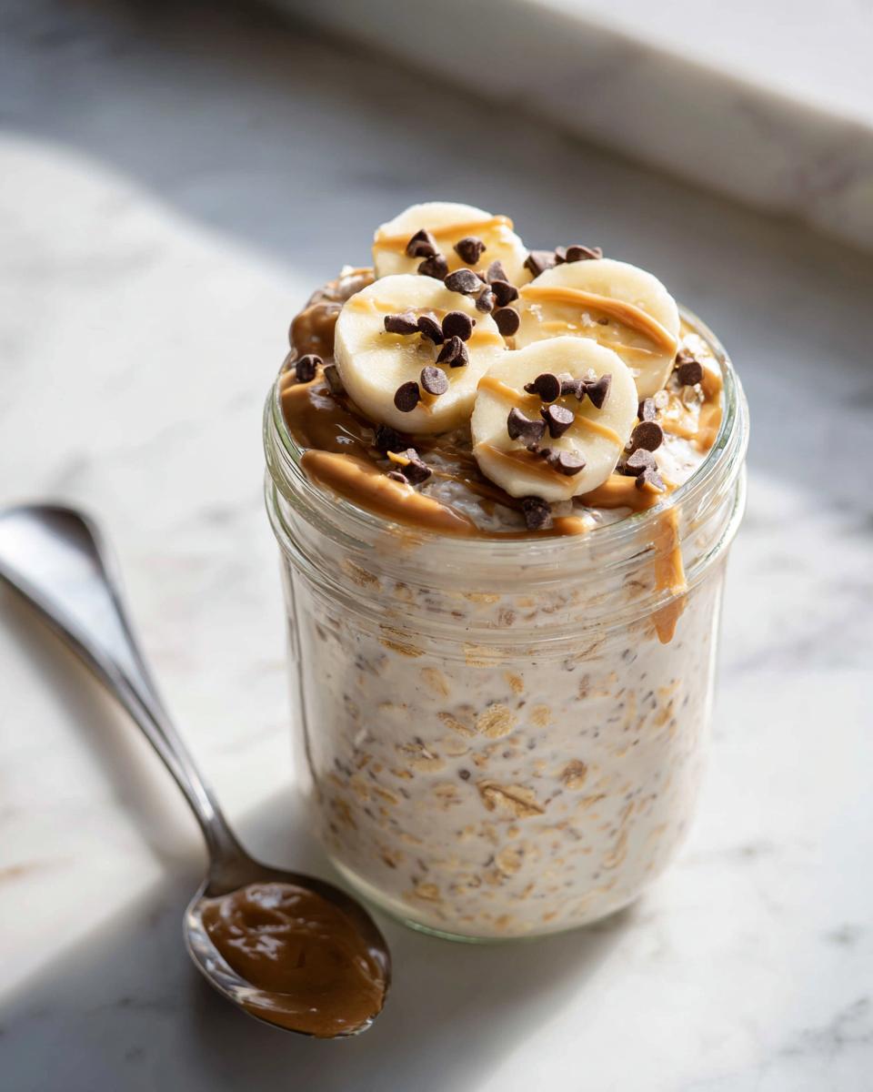 Close-up of Peanut Butter Banana Cinnamon Overnight Oats topped with banana slices, peanut butter drizzle, and chocolate chips.