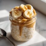 Close-up of Peanut Butter Banana Protein Overnight Oats topped with sliced bananas and cinnamon in a glass jar.