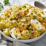 A creamy bowl of Southern Potato Salad with Eggs, garnished with paprika and fresh parsley.