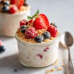 Close-up of Strawberry Cheesecake Oats topped with fresh strawberries, blueberries, raspberries, and graham cracker crumbs.