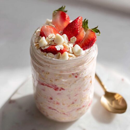 Close-up of Strawberry Cheesecake Overnight Oats with White Chocolate chips and fresh strawberries in a jar.