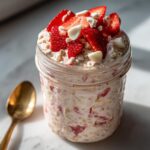 Close-up of Strawberry Cheesecake Overnight Oats with White Chocolate served in a glass jar, topped with fresh strawberries.