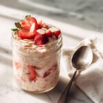 Close-up of Strawberry High-Protein Overnight Oats topped with fresh strawberries and slivered almonds in a glass jar.