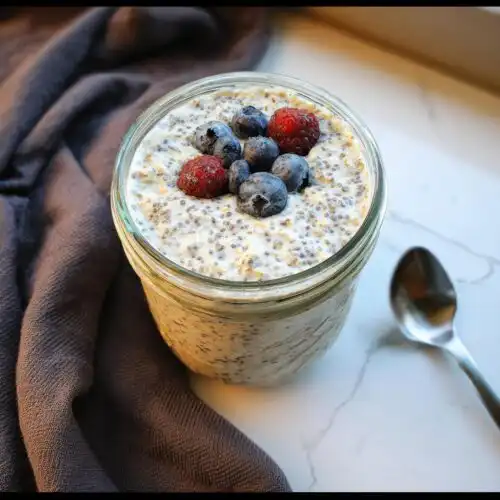 Close-up of Vanilla Chia Overnight Oats topped with fresh blueberries and raspberries in a glass jar.