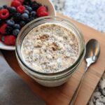 Overhead view of Vanilla Chia Overnight Oats in a glass jar, topped with cinnamon, next to fresh berries.