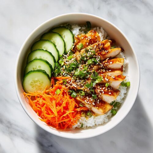 Overhead view of a Cold Chicken Rice Bowl featuring sliced glazed chicken, rice, cucumber, and shredded carrots.