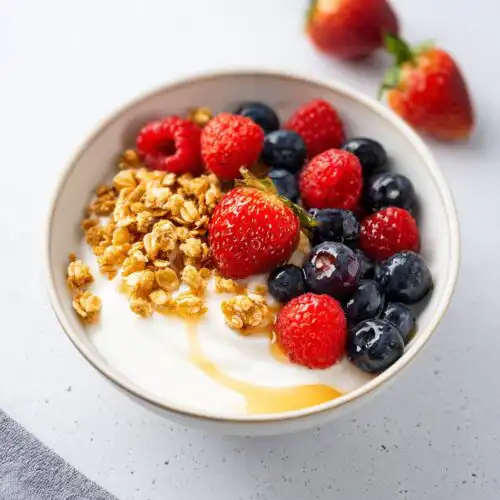 Close-up of an aesthetic Yogurt Bowl with Fruits, featuring strawberries, blueberries, raspberries, granola, and a drizzle of honey.