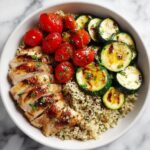 Overhead view of a Chicken Summer Plate featuring sliced grilled chicken, roasted tomatoes, grilled zucchini, and quinoa.