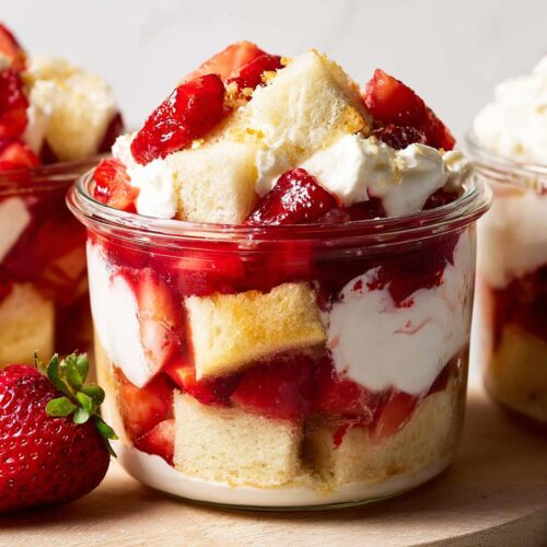 Close-up of layered Strawberry Shortcake Cups in a glass jar with cake, whipped cream, and macerated strawberries.