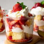 Close-up of a serving of Strawberry Shortcake Cups layered with cake, macerated strawberries, and whipped cream, topped with a whole berry.