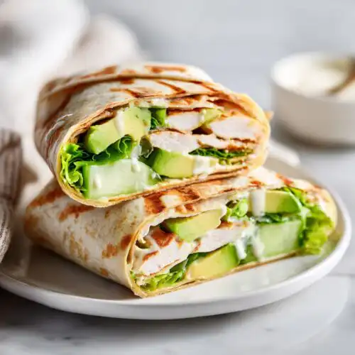 Two halves of a grilled wrap sandwich stacked, showing chicken, avocado, lettuce, and dressing, perfect for a picnic.