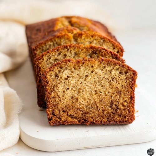 Close-up of several thick slices of moist Bakery Style Banana Bread on a white cutting board.