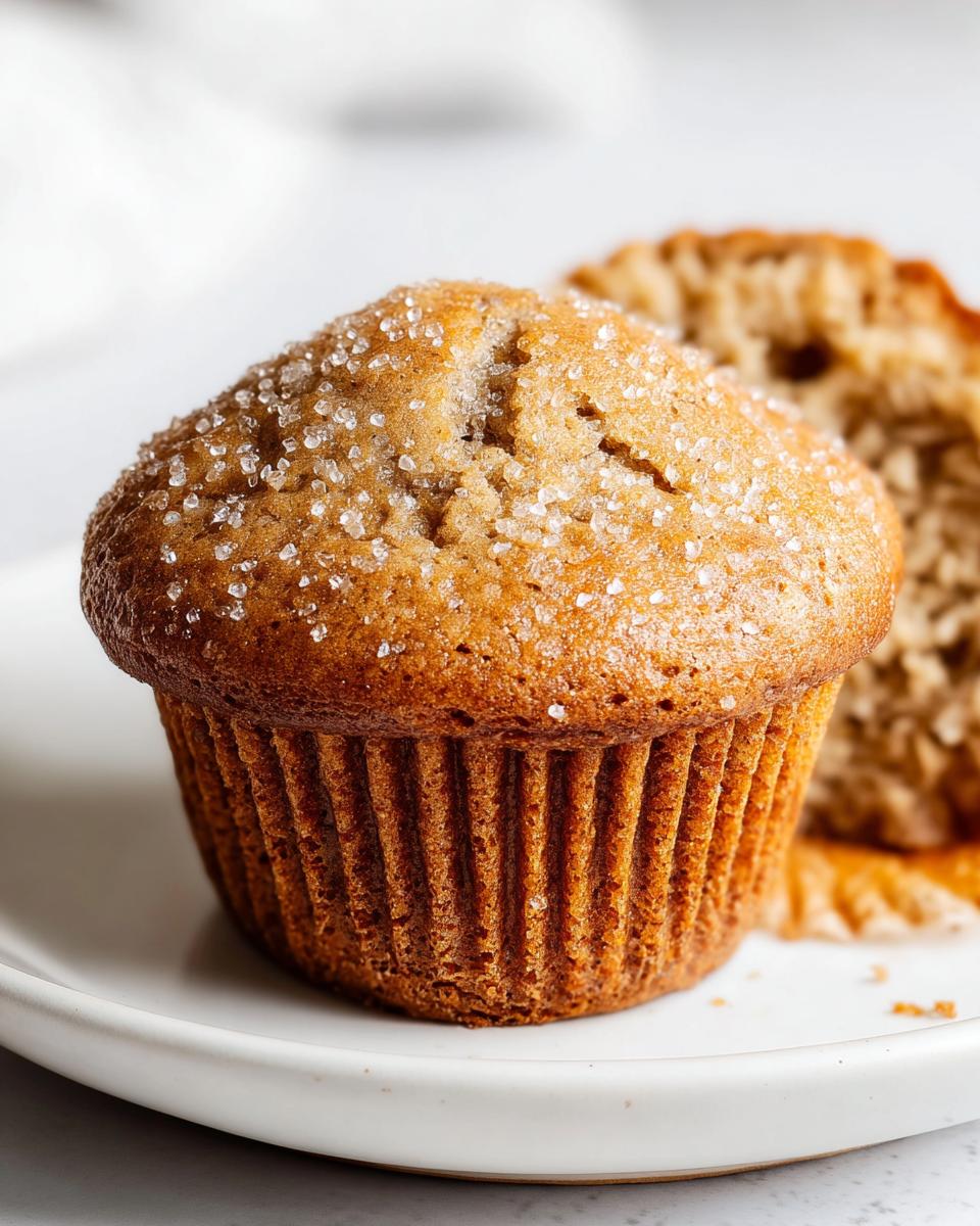 Close-up of a moist Banana Muffins Bakery Style topped with coarse sugar crystals on a white plate.