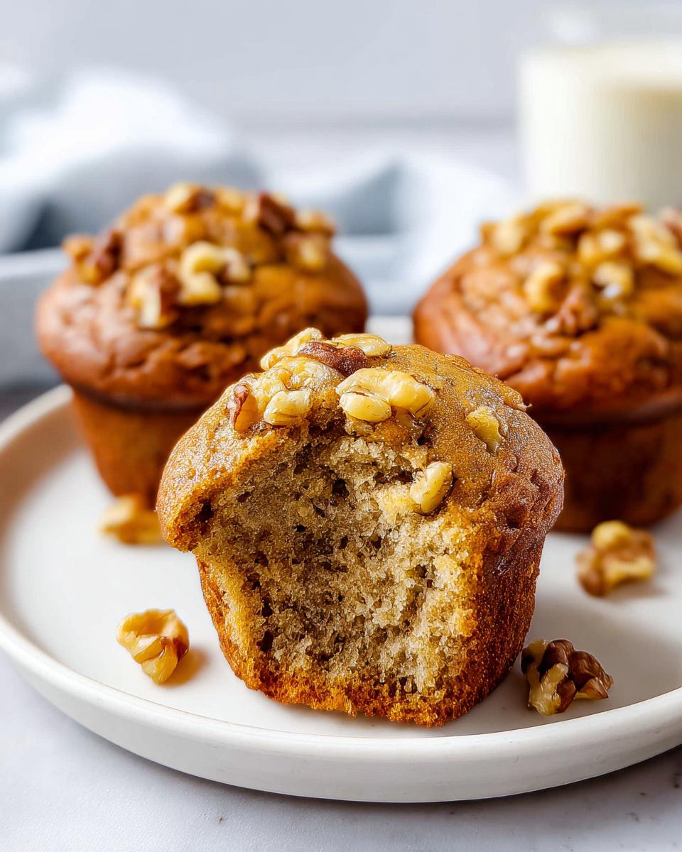 Close-up of a moist Banana Nut Muffin with a bite taken out, showing the texture and topped with walnuts.
