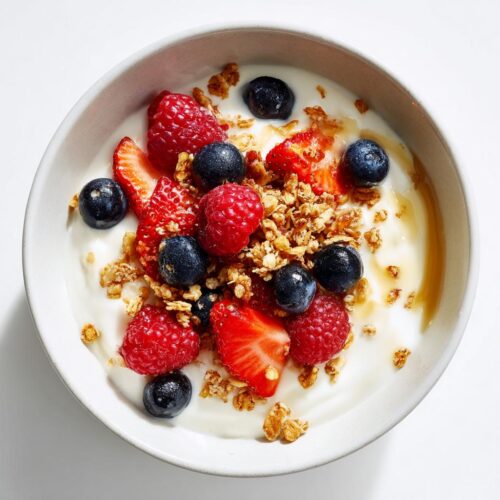 Overhead view of a vibrant Berry Breakfast Bowl featuring yogurt, fresh raspberries, blueberries, sliced strawberries, and crunchy granola.