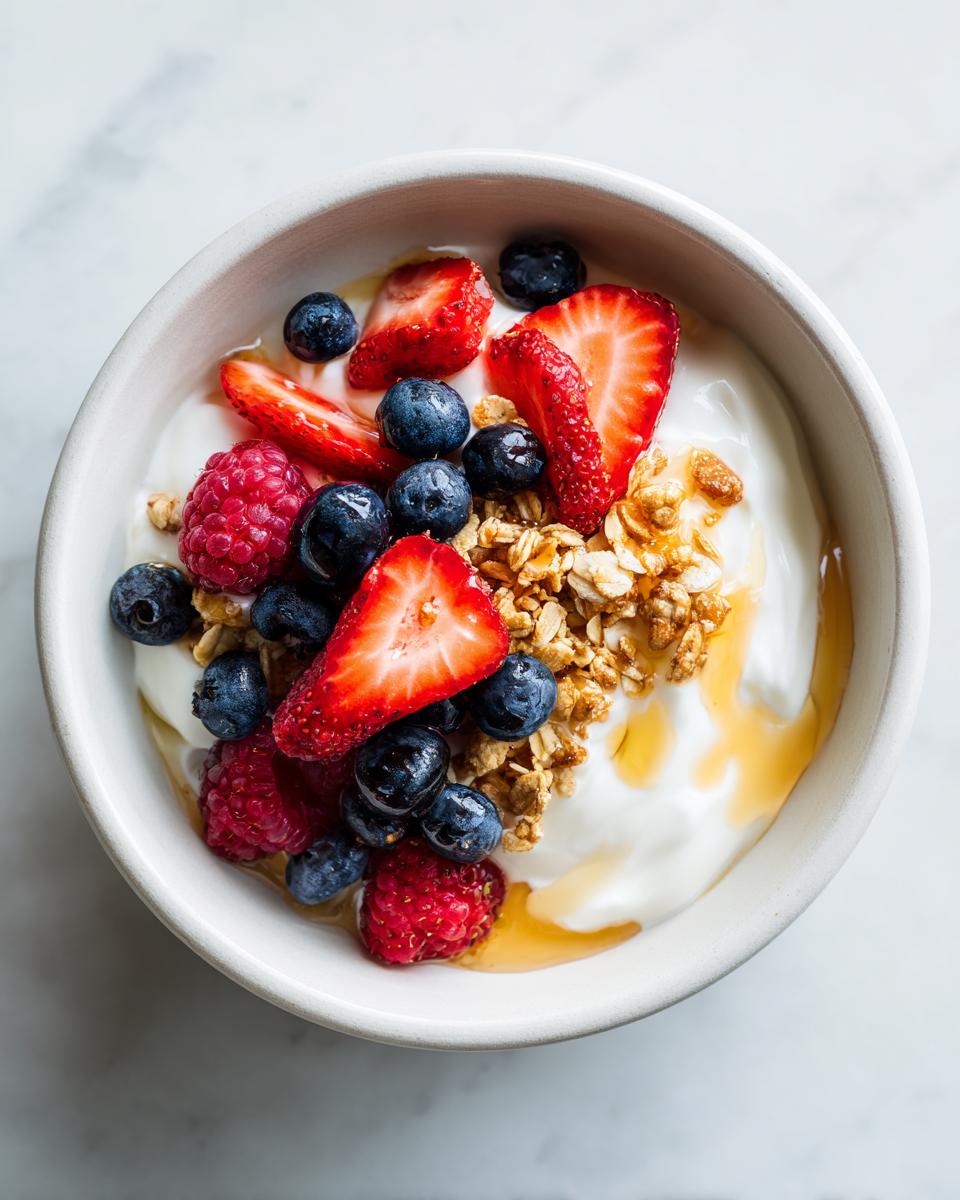 Overhead view of a vibrant Berry Breakfast Bowl featuring yogurt, fresh strawberries, blueberries, raspberries, granola, and a drizzle of honey.
