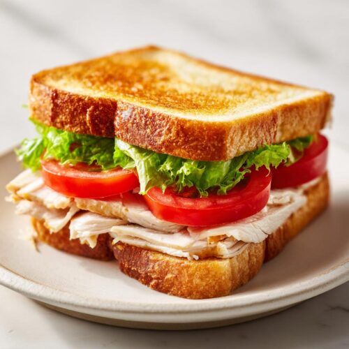 A close-up of a delicious Chicken Sandwich Picnic made with toasted bread, sliced white chicken, bright red tomatoes, and crisp lettuce.