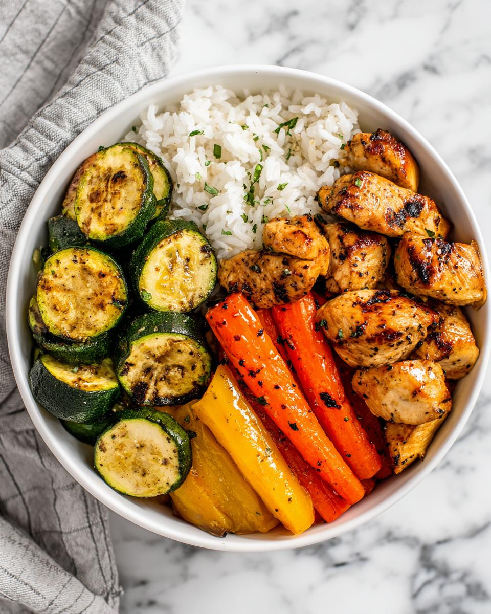 Overhead view of a Chicken Veggie Summer Bowl featuring grilled chicken, rice, grilled zucchini, and roasted carrots.