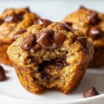 Close-up of a Chocolate Chip Banana Muffins with a bite taken out, showing gooey melted chocolate chips inside.