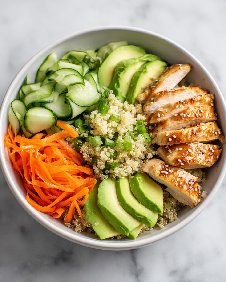 Overhead view of a Cold Chicken Bowl featuring sliced chicken breast, quinoa, avocado, shredded carrots, and ribbons of cucumber.