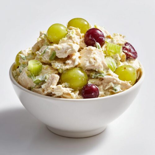 A white bowl filled with creamy Cold Chicken Salad Meal Prep mixed with celery and topped with red and green grapes.