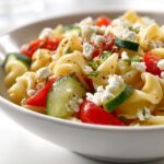 A close-up of a vibrant Cold Pasta Salad Lunch featuring rotini pasta, cherry tomatoes, cucumber slices, and crumbled feta cheese.